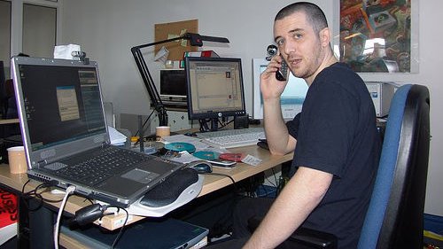un homme à son bureau de travail encombré d'ordinateurs est en train de téléphoner
