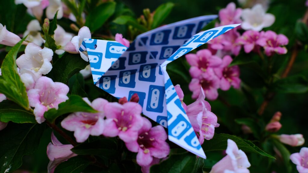 Origami papillon réalisé avec une feuille portant des logos de Castopod, posé sur des fleurs