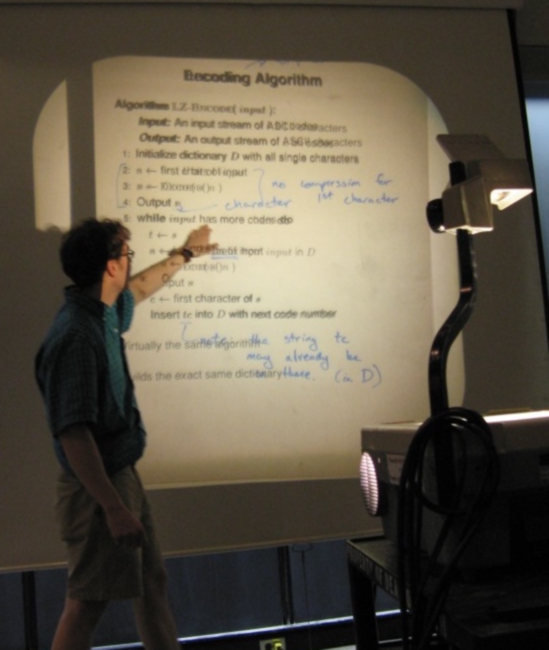 un jeune homme montre une ligne d'une explication de l'encodage des algorithmes au rétroprojecteur 