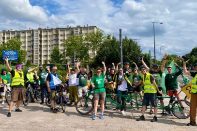 Photo d'un foule de personnes en ville habillées aux couleurs vertes d'Alternatiba et avec de nombreux vélos et quelques drapeaux, levant la main.