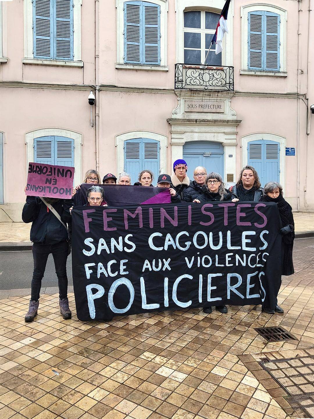 Action de la collective écoféministe Les chouettes effraient : des femmes posent derrière une banderole « FÉMINISTES SANS CAGOULES FACE AUX VIOLENCES POLICIÈRES » et une femme tient devant son visage, à l'envers, une pancarte HOOLIGANS EN UNIFORME